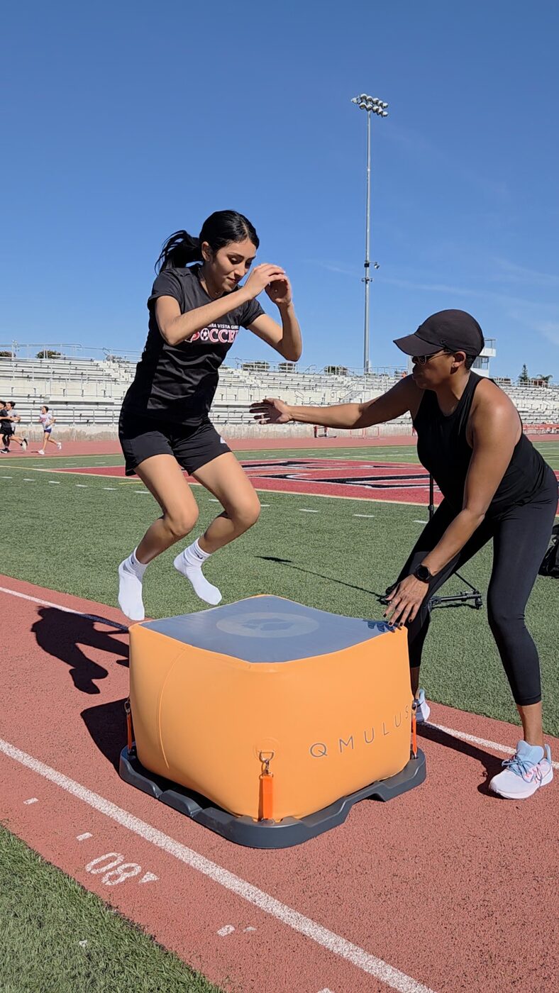 An athlete driving up onto a plyo box during a track session as Coach Peters coaches.